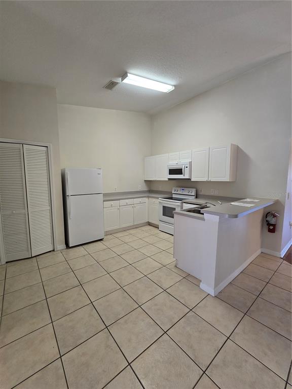 A kitchen features white cabinets, white appliances, a breakfast bar, and light-colored tile flooring — 2790 CLUB CORTILE CIRCLE UNIT B, KISSIMMEE, FL