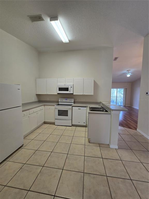 A kitchen with white cabinets, white appliances, and beige tile flooring — 2790 CLUB CORTILE CIRCLE UNIT B, KISSIMMEE, FL
