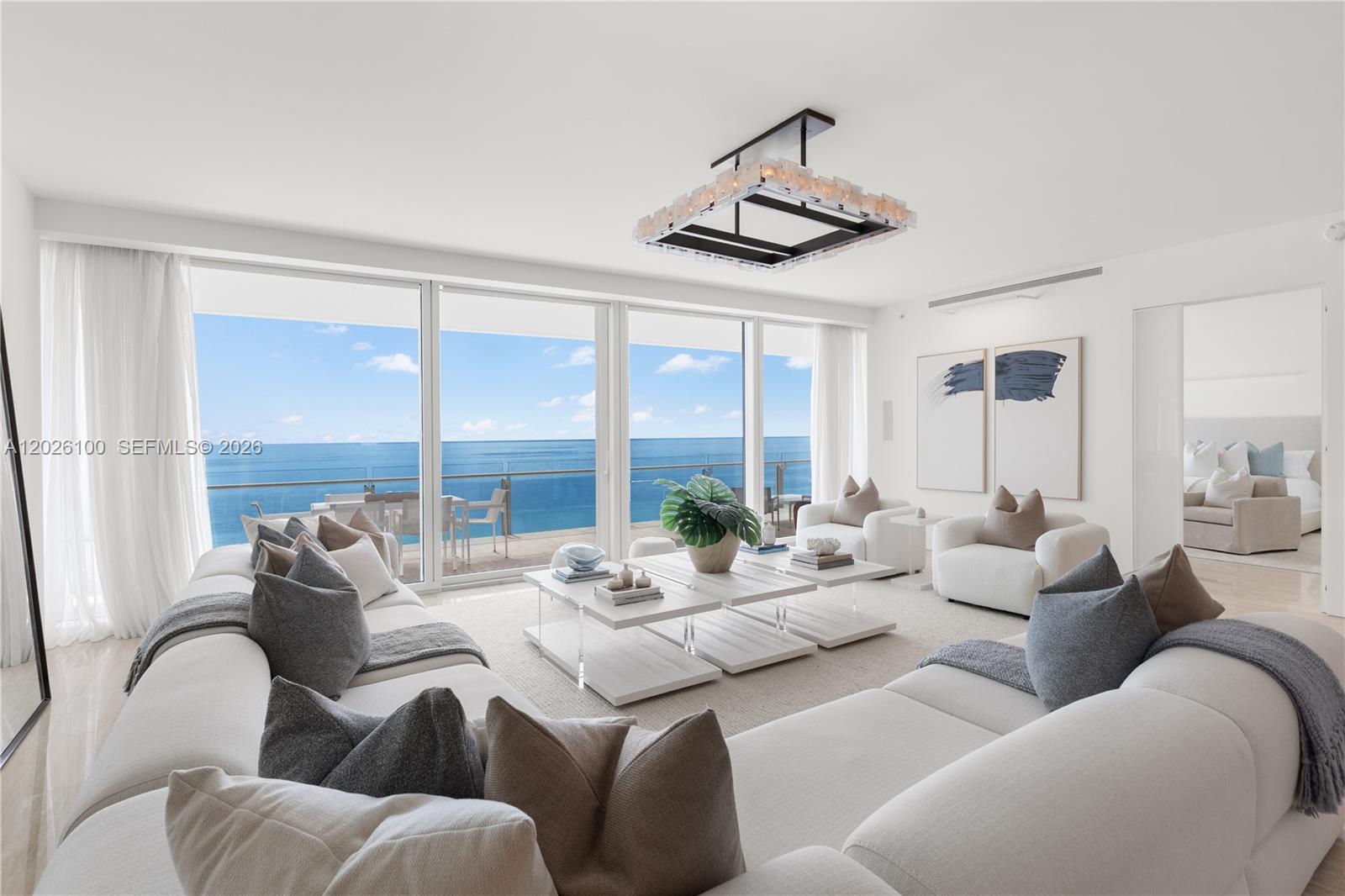 A bright living room features white sofas, a modern chandelier, and floor-to-ceiling ocean views — 9001 Collins Ave # 1003, Surfside FL 33154, SURFSIDE, FL