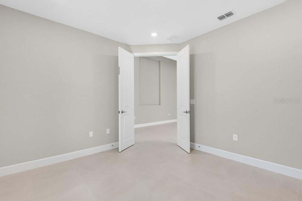 A room with light-colored tile flooring and double doors opening into another carpeted room — 10 GEOSAM DRIVE, PALM COAST, FL