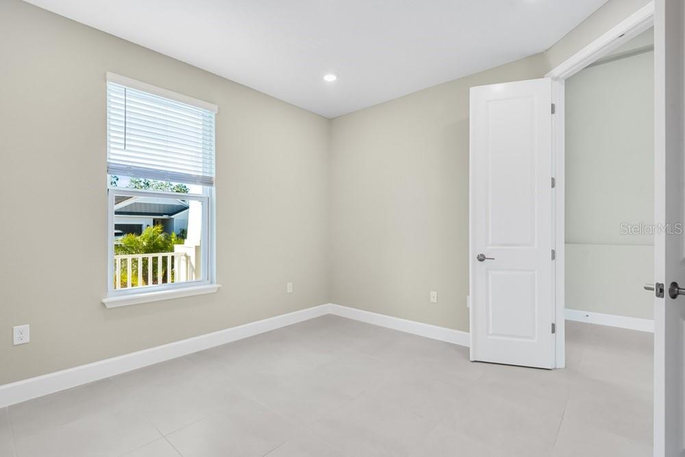 A bright bedroom with light-colored walls, large tile flooring, and a window overlooking a balcony — 10 GEOSAM DRIVE, PALM COAST, FL