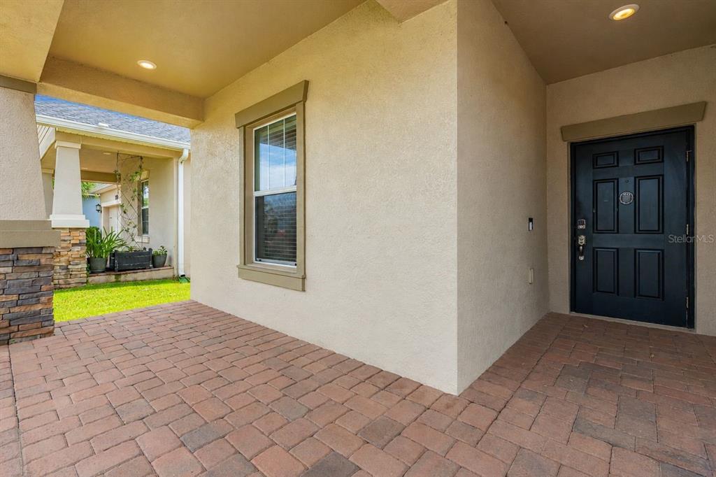 A covered entryway features a brick paver floor, a dark front door, and a window — 14157 GOLD BRIDGE DRIVE, ORLANDO, FL