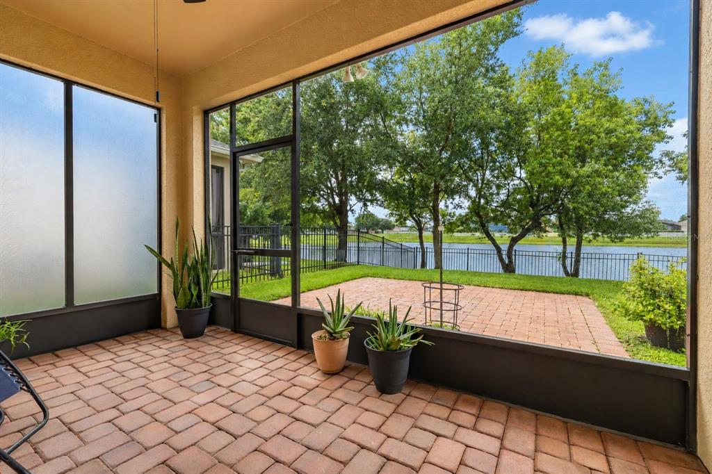 A screened-in patio with brick pavers overlooks a grassy yard, a metal fence, and water — 14157 GOLD BRIDGE DRIVE, ORLANDO, FL