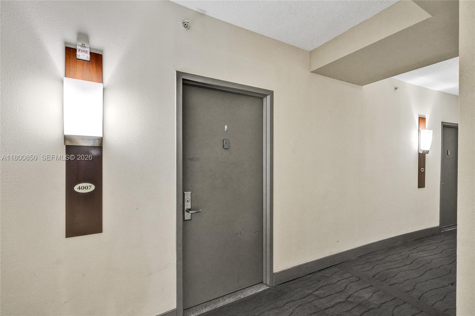 A hallway features a gray apartment door numbered 4007, wall-mounted light fixtures, and dark carpeting — 1750 N Bayshore Dr # 4007, Miami FL 33132, MIAMI, FL