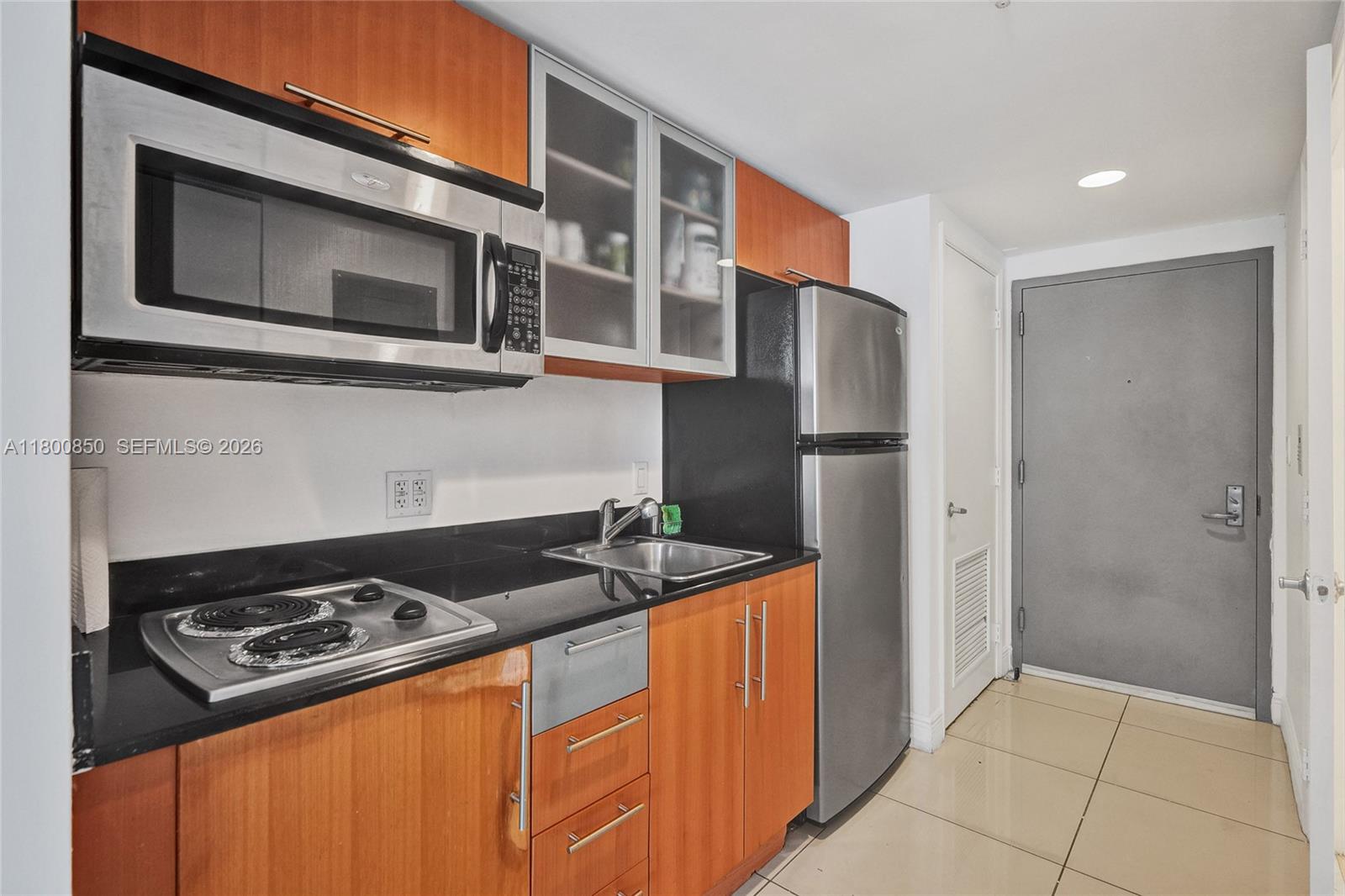 A compact kitchen features wood cabinets, black countertops, stainless steel appliances, and tile flooring — 1750 N Bayshore Dr # 4007, Miami FL 33132, MIAMI, FL