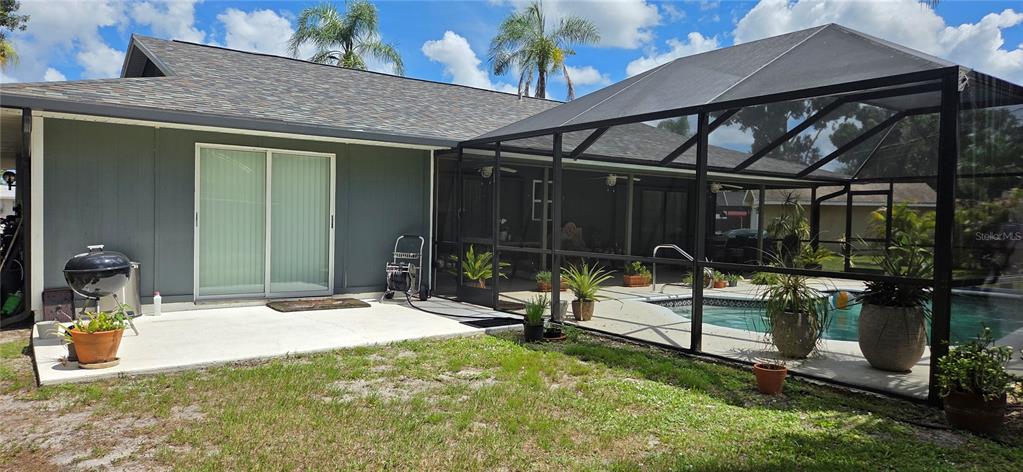 A backyard features a concrete patio, a charcoal grill, and a screened-in swimming pool enclosure — 221 DADE AVENUE, SARASOTA, FL