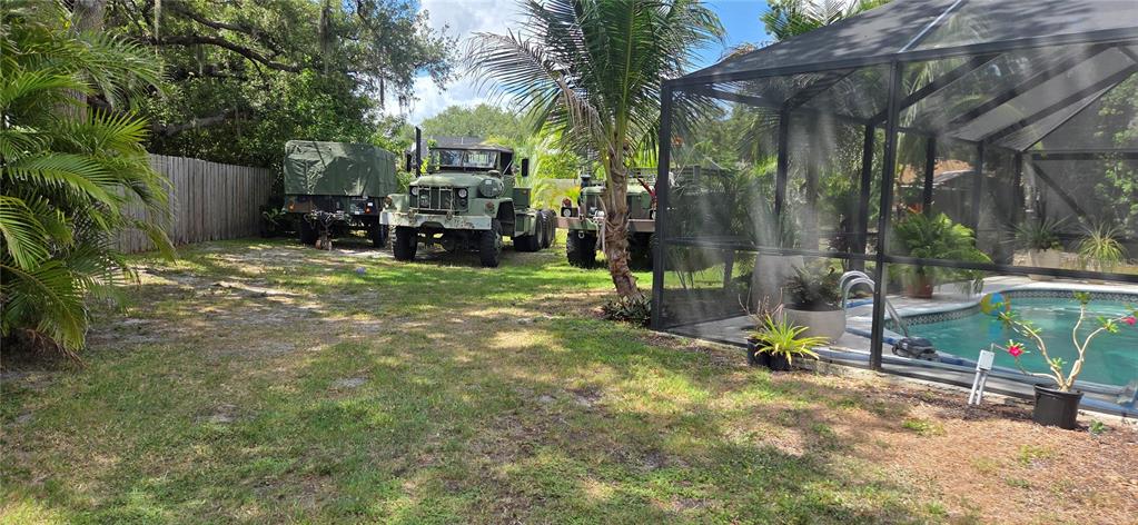 A backyard features a swimming pool with a screen enclosure and two military trucks parked — 221 DADE AVENUE, SARASOTA, FL