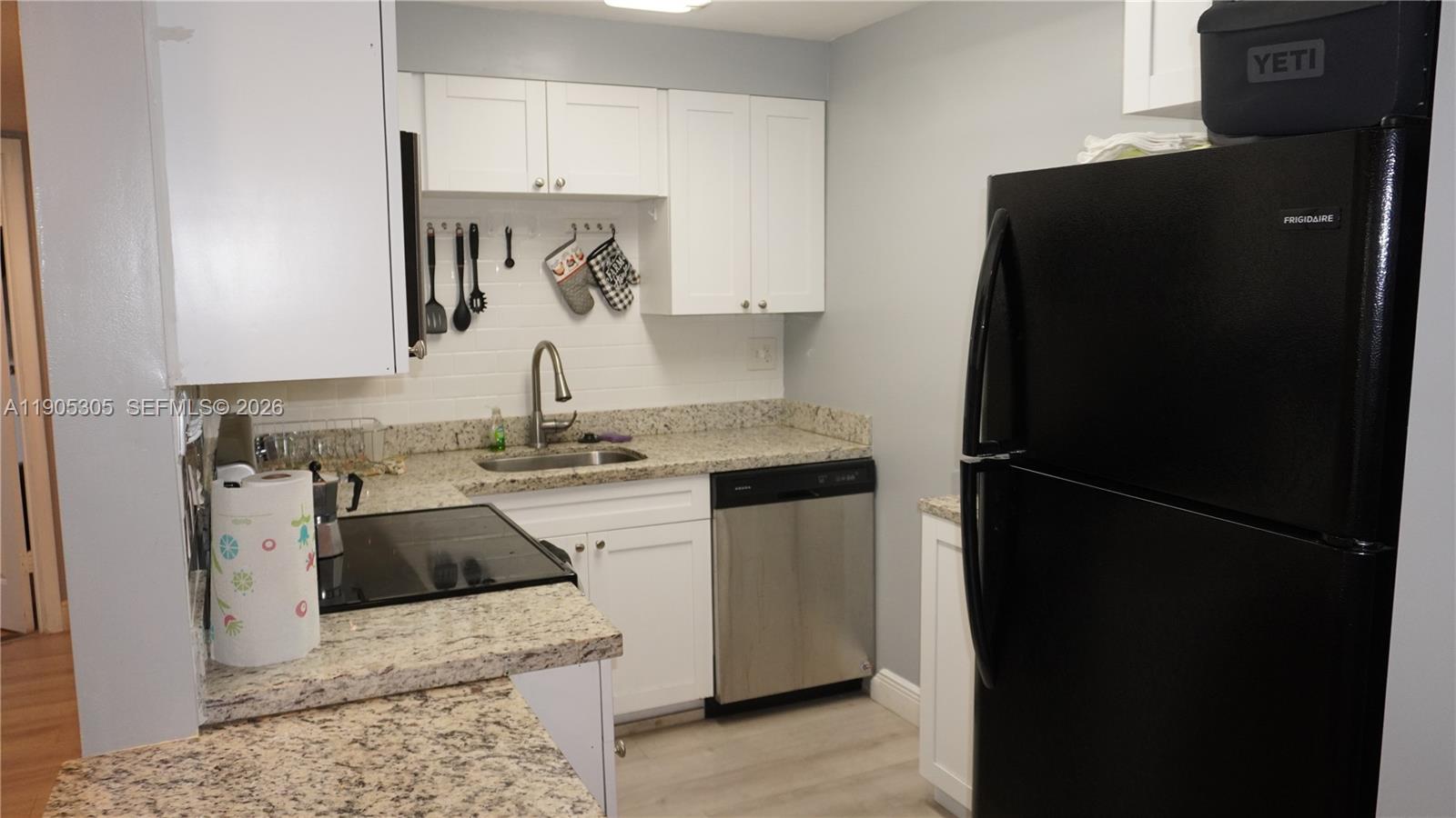 A kitchen features white cabinets, granite countertops, a stainless steel dishwasher, and a black refrigerator — 3710 N Pine Island Rd # 320, Sunrise FL 33351, SUNRISE, FL