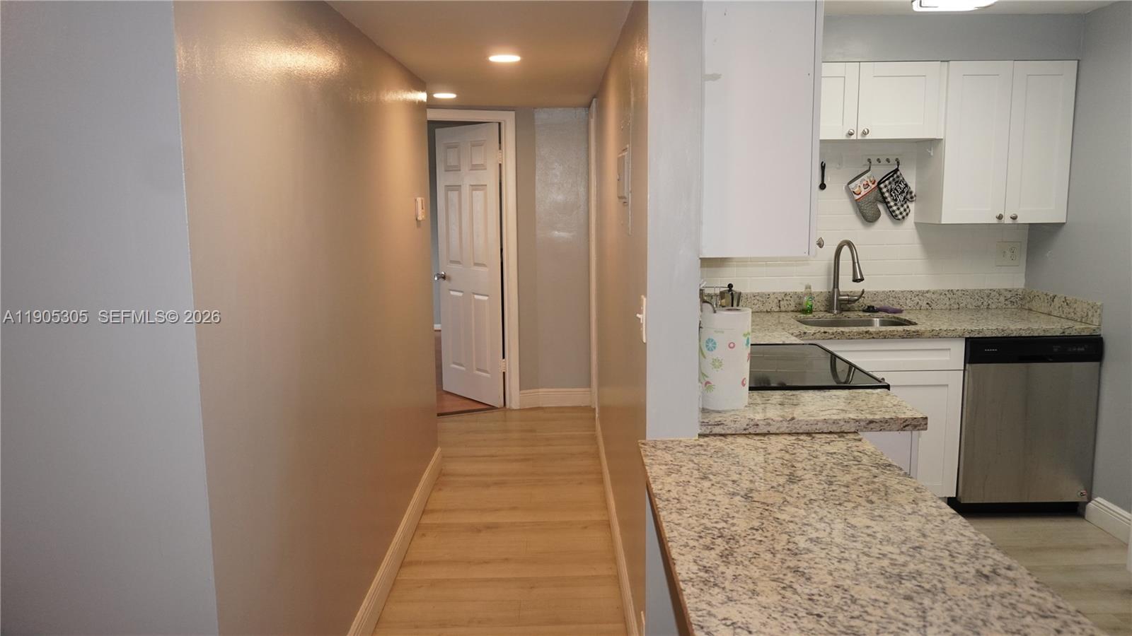 A kitchen with granite countertops and white cabinets opens into a hallway with wood flooring — 3710 N Pine Island Rd # 320, Sunrise FL 33351, SUNRISE, FL