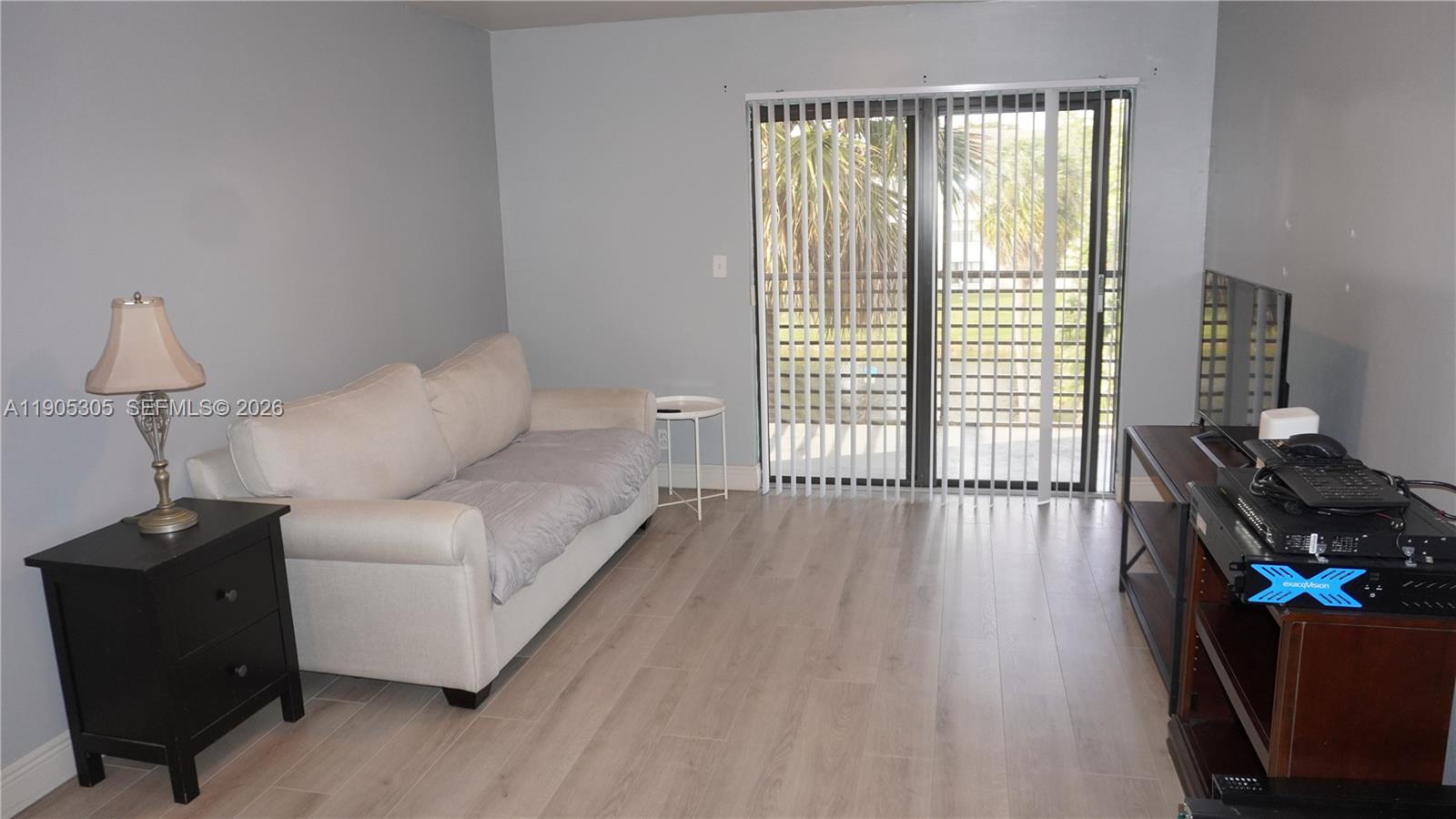 A living room features light wood-look flooring, a beige sofa, a black end table, and a sliding glass door — 3710 N Pine Island Rd # 320, Sunrise FL 33351, SUNRISE, FL