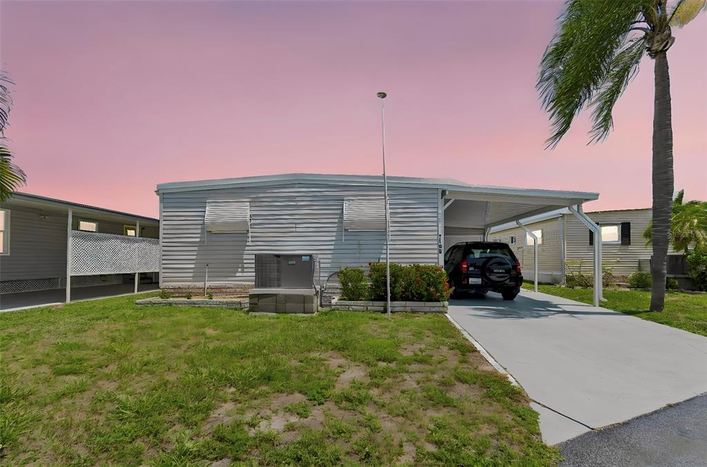 A single-story manufactured home with a carport, driveway, and lawn under a pink sky — 7186 MOUNT ARLINGTON DRIVE NE UNIT 421, ST PETERSBURG, FL