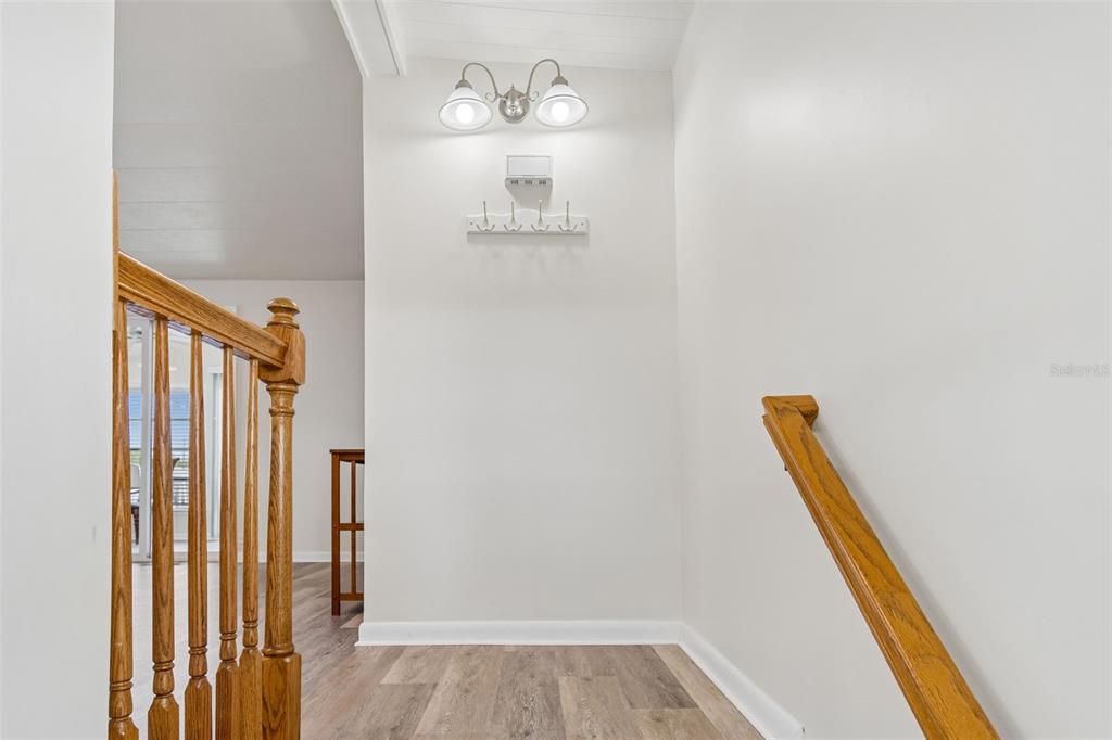 A staircase landing features light wood-look flooring, white walls, a coat rack, and wall lighting — 7186 MOUNT ARLINGTON DRIVE NE UNIT 421, ST PETERSBURG, FL