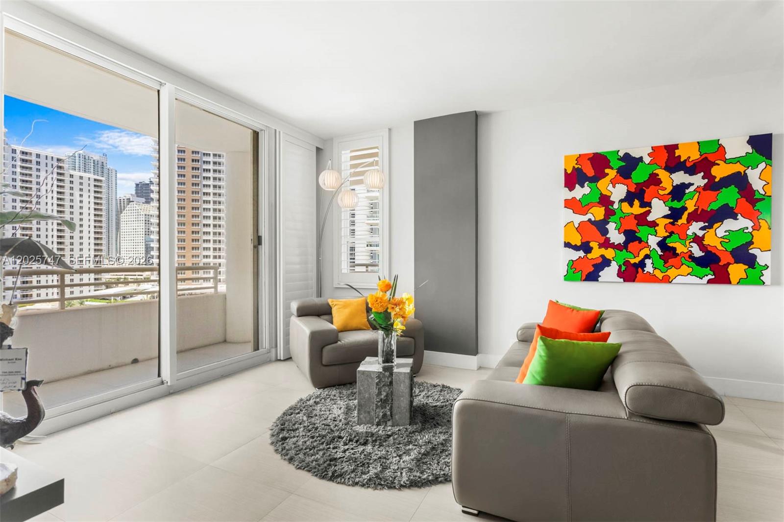 A modern living room features gray leather furniture, a colorful abstract painting, and a balcony view — 888 Brickell Key Dr # 1002, Miami FL 33131, MIAMI, FL