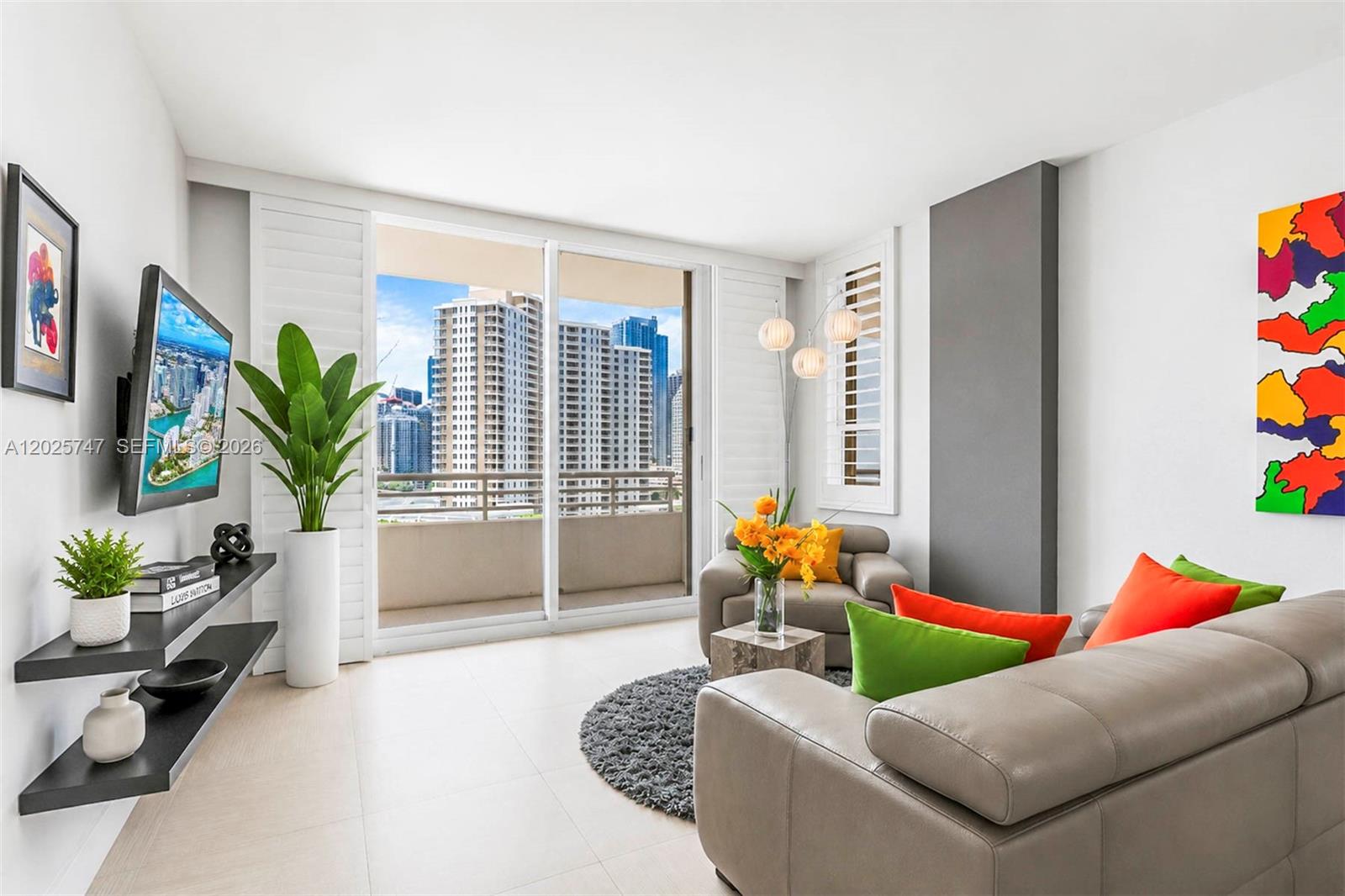 A modern living room features a gray sofa, wall-mounted television, and a balcony with city views — 888 Brickell Key Dr # 1002, Miami FL 33131, MIAMI, FL