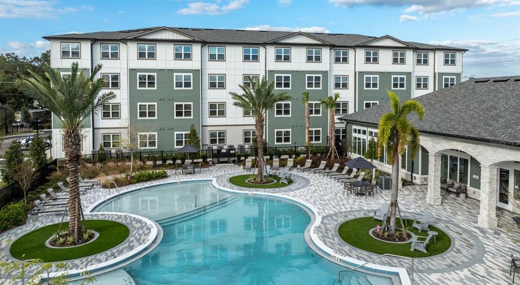 An outdoor swimming pool with lounge chairs and palm trees sits before a large apartment building — 10881 CALADESI AVENUE UNIT A2, TAMPA, FL