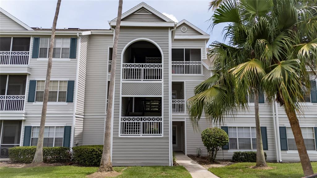 A three-story apartment building with light-colored siding, screened balconies, and palm trees in front — 5017 CITY STREET UNIT 1938, ORLANDO, FL