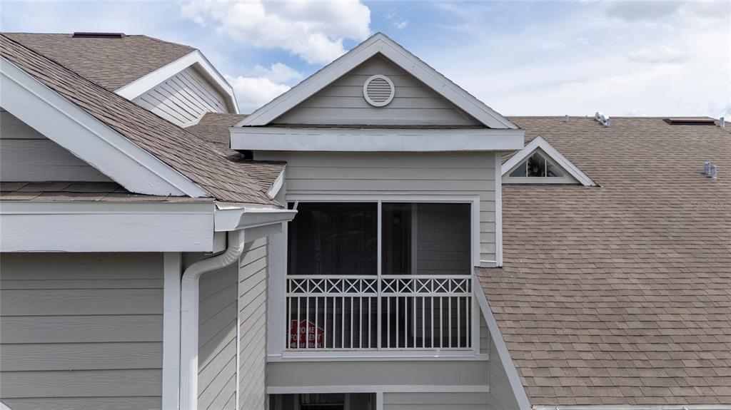 An exterior view of a house featuring a screened-in balcony and a gabled roof — 5017 CITY STREET UNIT 1938, ORLANDO, FL