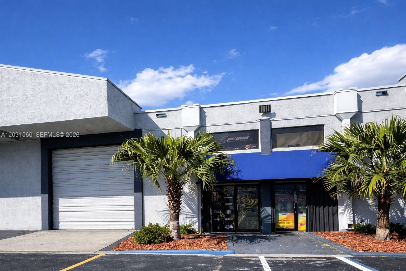A low-rise commercial building features a roll-up garage door, glass storefronts, and two palm trees — 5501 NW 74th Ave # 5501, Miami FL 33166, MIAMI, FL