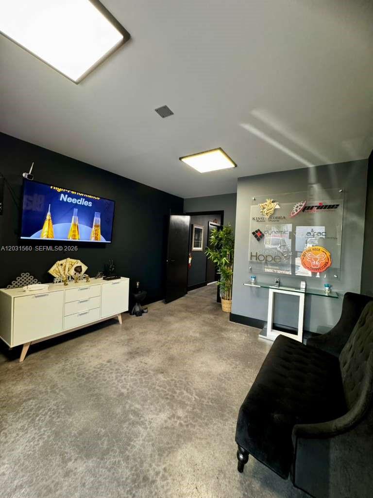 A waiting room features a black accent wall, concrete floors, a television, and a reception desk — 5501 NW 74th Ave # 5501, Miami FL 33166, MIAMI, FL