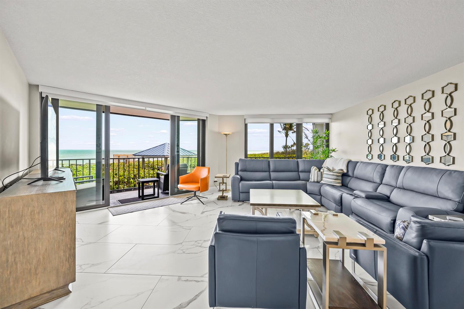A living room features a blue sectional sofa, marble-look tile floors, and a balcony view — 9650 S Ocean Drive # 106, Jensen Beach FL 34957, JENSEN BEACH, FL