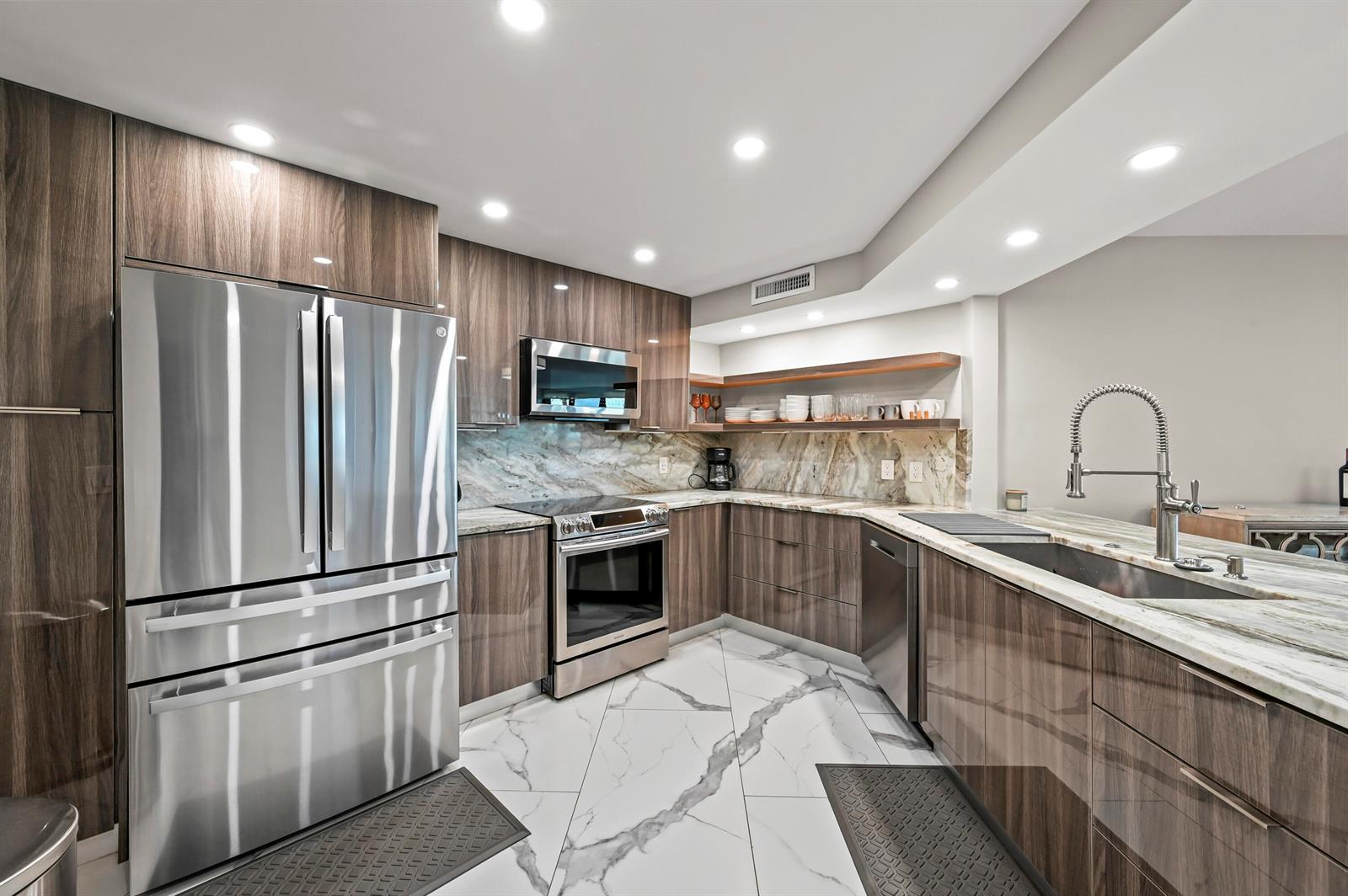 A modern kitchen features wood-grain cabinets, marble countertops, stainless steel appliances, and white marble flooring — 9650 S Ocean Drive # 106, Jensen Beach FL 34957, JENSEN BEACH, FL