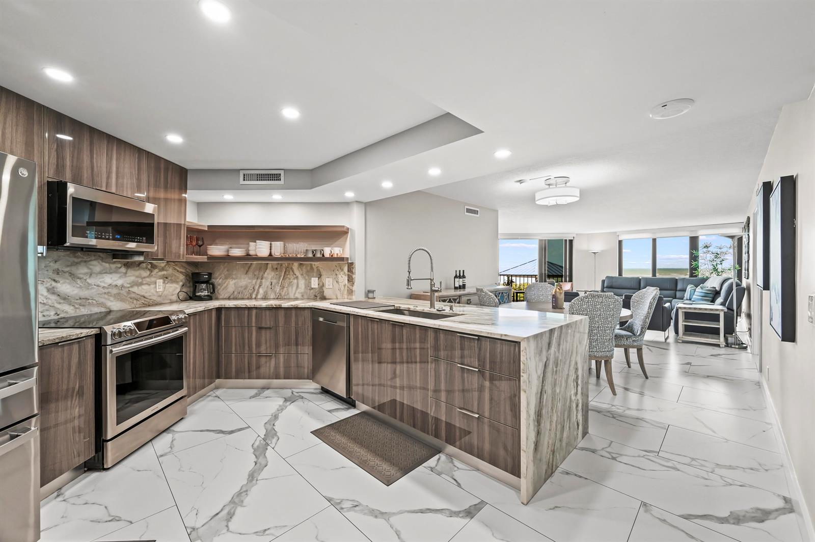 A modern kitchen with wood cabinets and marble countertops opens into a dining and living area — 9650 S Ocean Drive # 106, Jensen Beach FL 34957, JENSEN BEACH, FL