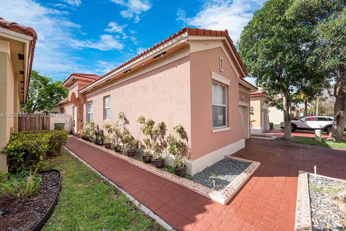 A side view of a peach-colored house with a red brick walkway and potted plants — 2327 NE 37th Ter, Homestead FL 33033, HOMESTEAD, FL