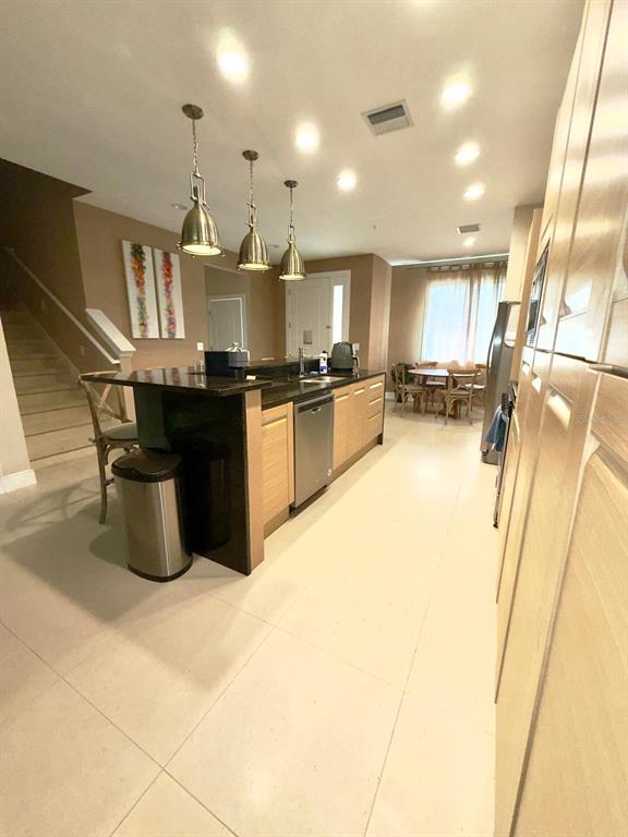 A kitchen features a dark island with pendant lights, light wood cabinets, and tile flooring — 7657 RECIFE DRIVE, KISSIMMEE, FL