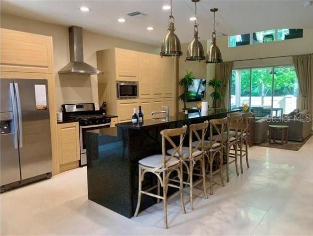 A modern kitchen features light wood cabinets, a black granite island, and three pendant lights — 7657 RECIFE DRIVE, KISSIMMEE, FL