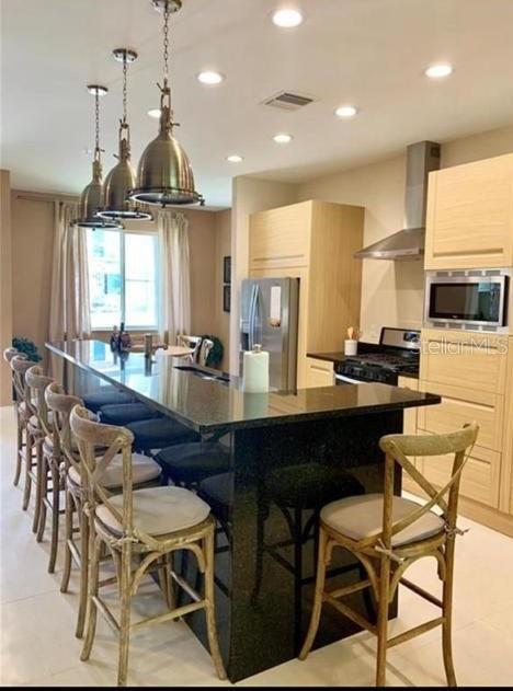 A kitchen features a dark granite island with wooden bar stools and pendant lighting — 7657 RECIFE DRIVE, KISSIMMEE, FL