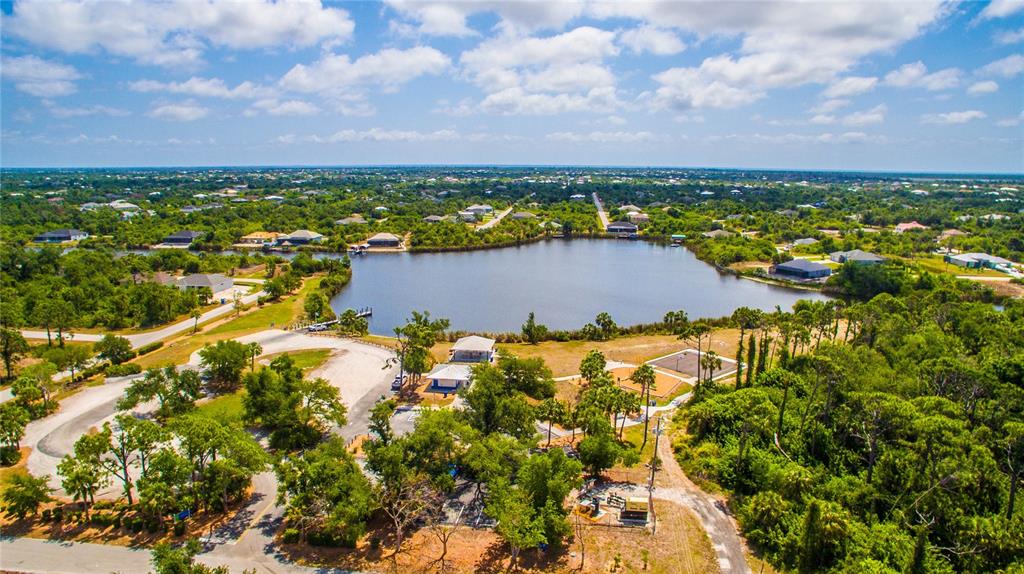 An aerial view shows a lake surrounded by trees, residential houses, and a parking area — 10017 COCOA BEACH STREET, PORT CHARLOTTE, FL