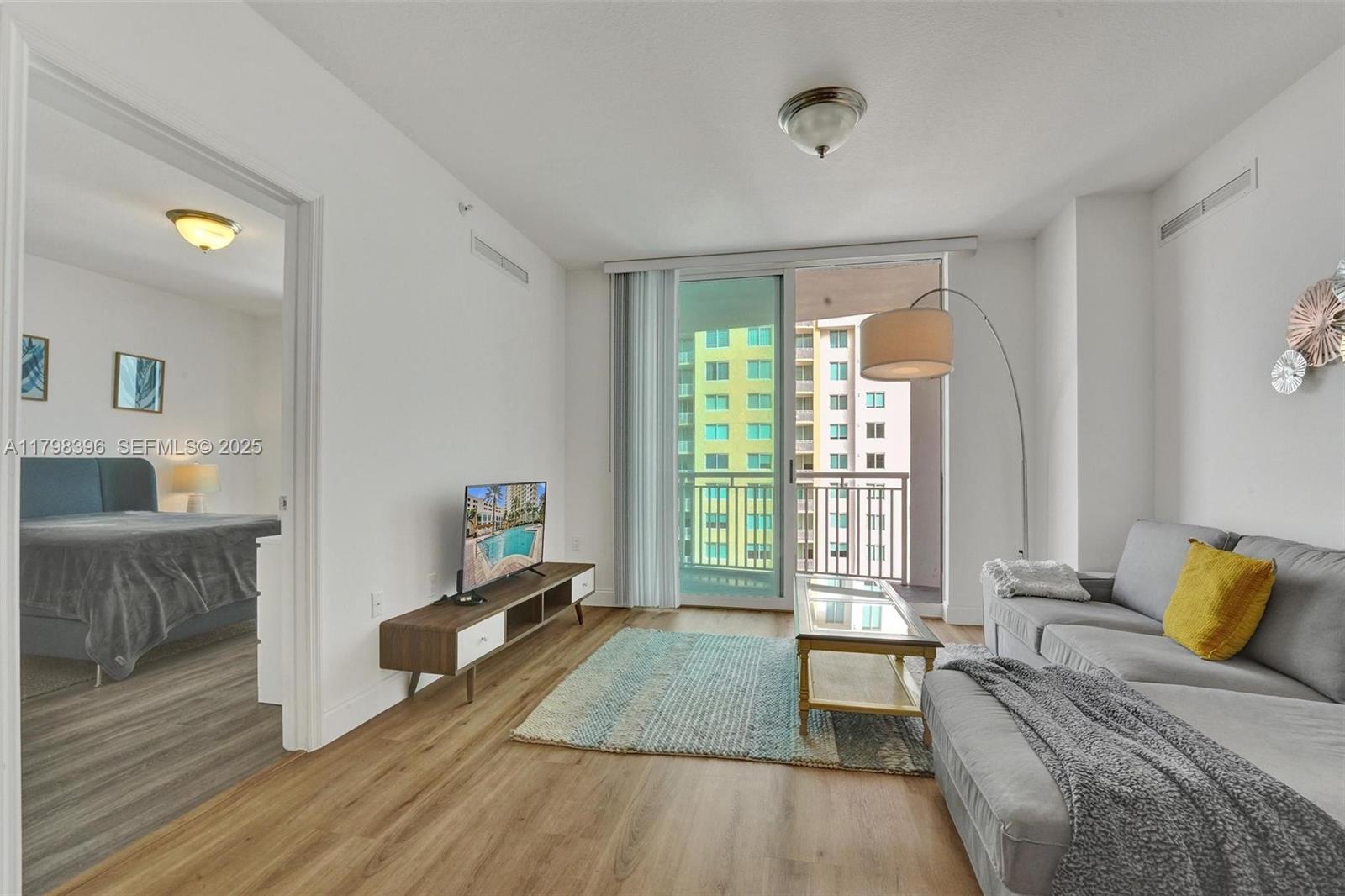 A living room with wood-look flooring, a grey sectional sofa, and a balcony view — 1745 E Hallandale Beach Blvd # 2105W, Hallandale Beach FL 33009, HALLANDALE BEACH, FL