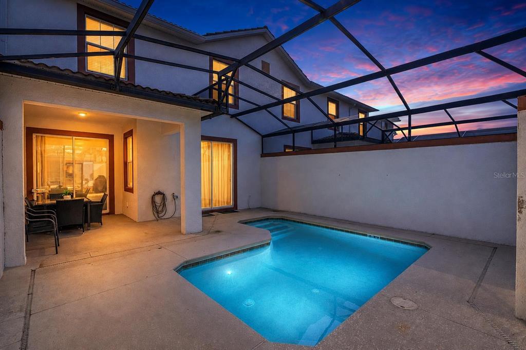 A backyard swimming pool with a screened enclosure sits beside a two-story house at dusk — 3080 JULIET DRIVE, KISSIMMEE, FL