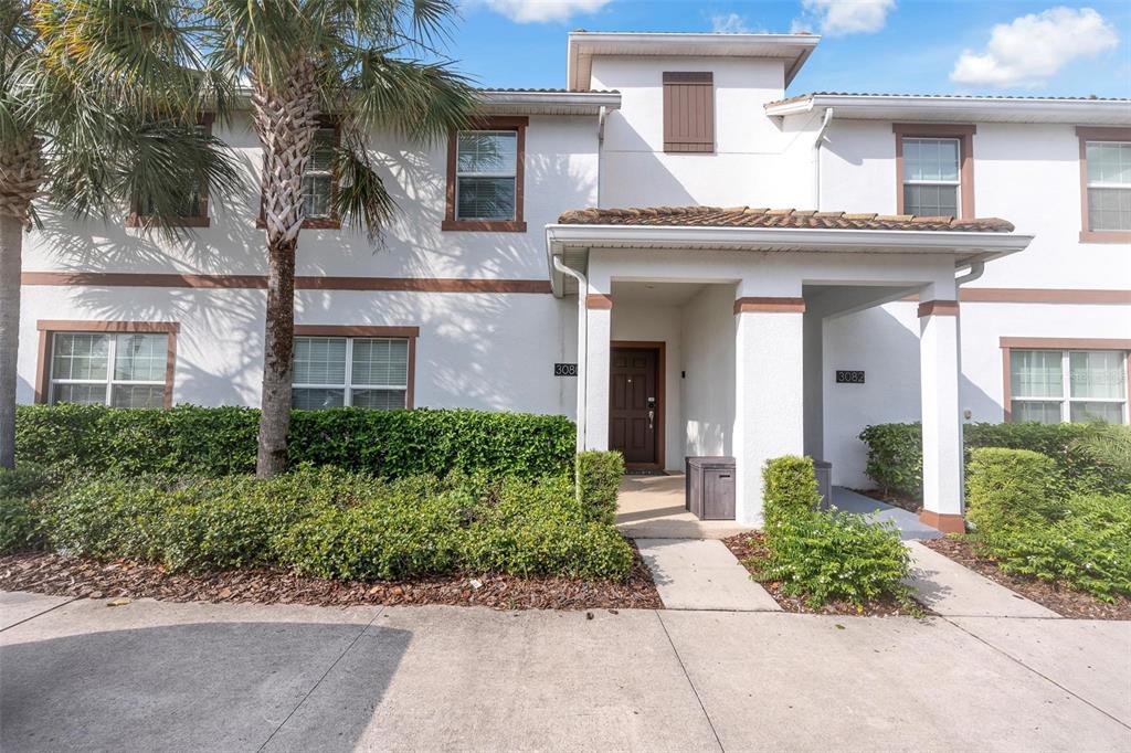 The exterior of a two-story townhouse features white stucco walls, brown trim, and a palm tree — 3080 JULIET DRIVE, KISSIMMEE, FL