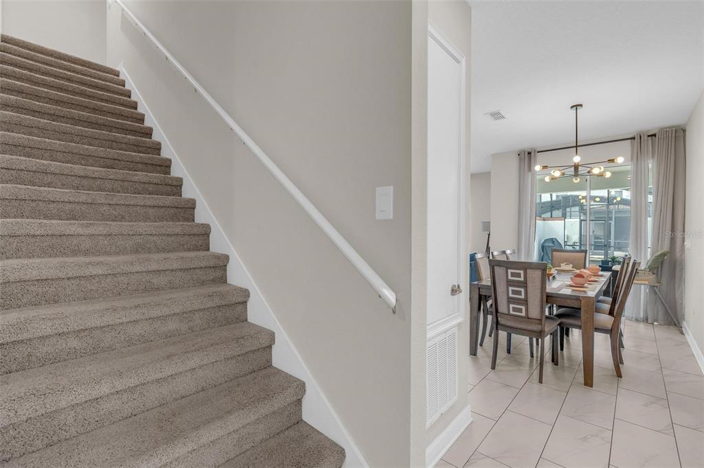 A carpeted staircase leads upward next to a dining area with a modern light fixture — 3080 JULIET DRIVE, KISSIMMEE, FL