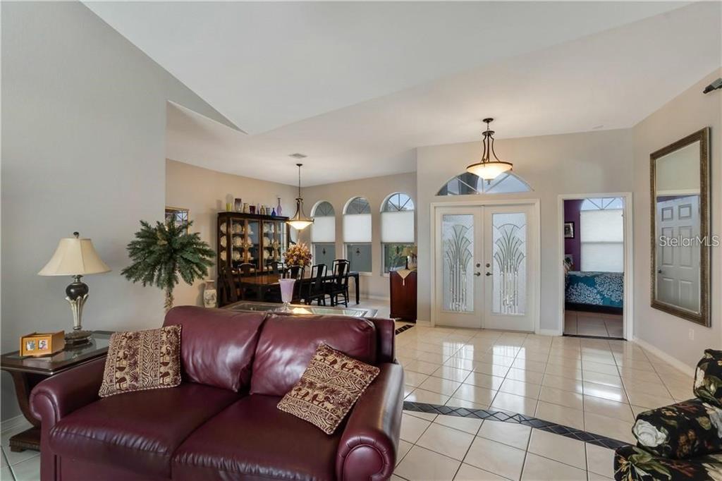 A living room with tile floors, a burgundy sofa, and a dining area in the background — 15352 POTTSTOWN AVENUE, PORT CHARLOTTE, FL