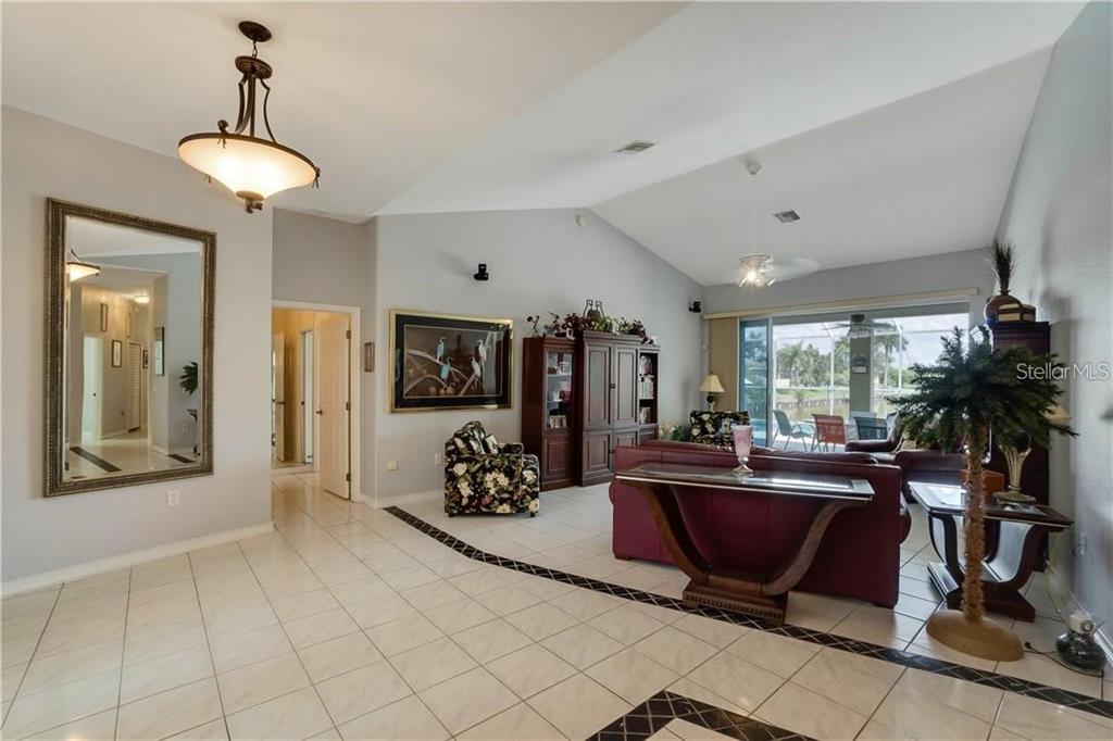 A spacious living room with vaulted ceilings, tile floors, and a view of a pool — 15352 POTTSTOWN AVENUE, PORT CHARLOTTE, FL