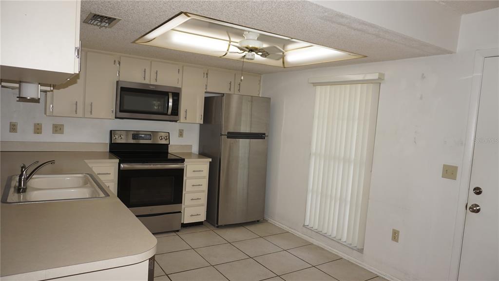 A kitchen features white cabinets, stainless steel appliances, a tiled floor, and a ceiling light — 12543 DEARBORN DRIVE, HUDSON, FL