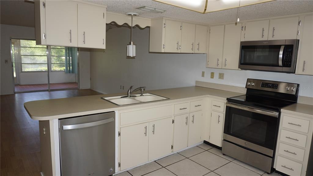 A kitchen features off-white cabinets, stainless steel appliances, and a peninsula with a double sink — 12543 DEARBORN DRIVE, HUDSON, FL
