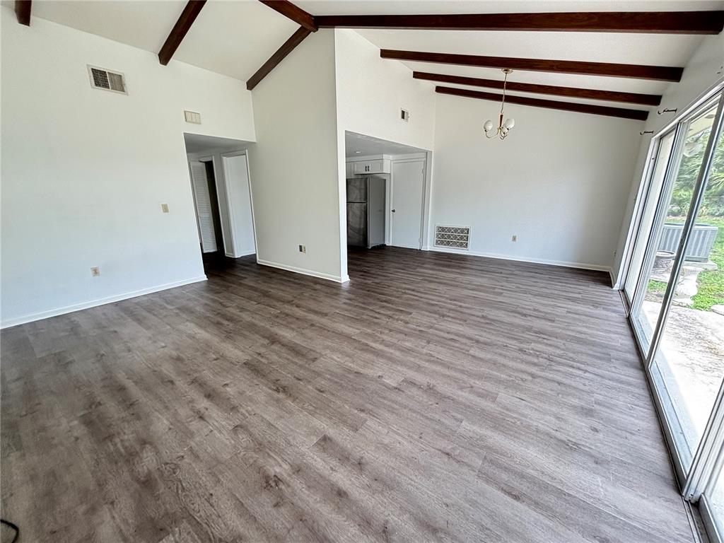 An open-concept living area features vaulted ceilings with exposed wooden beams and gray flooring — 8302 N FLINTROCK COURT, TAMPA, FL