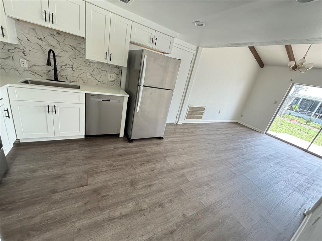 A kitchen with white cabinets, stainless steel appliances, and wood-look flooring opens to a living area — 8302 N FLINTROCK COURT, TAMPA, FL