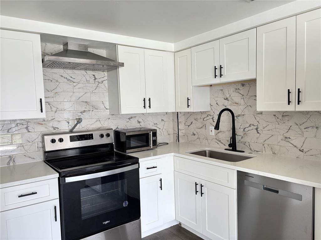 A kitchen features white cabinets, marble-patterned tile backsplash, stainless steel appliances, and quartz countertops — 8302 N FLINTROCK COURT, TAMPA, FL