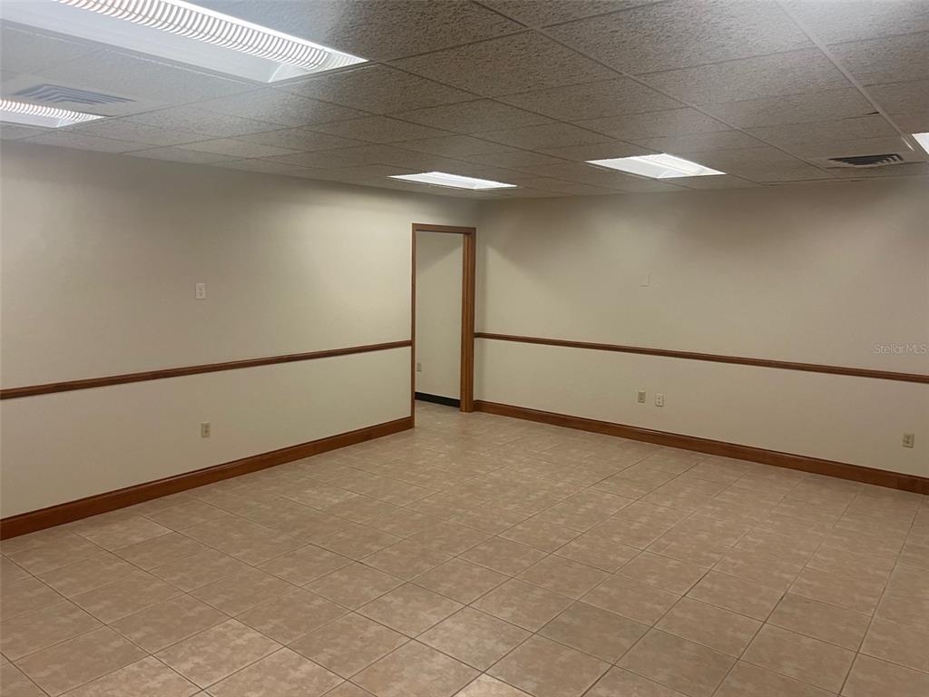 An empty room with beige tile flooring, white walls, chair rail molding, and drop ceiling lights — 3501 SW 2ND AVENUE UNIT 2300, GAINESVILLE, FL
