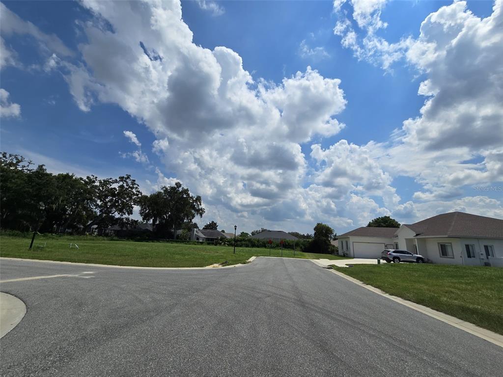 A paved cul-de-sac street borders a grassy vacant lot next to a suburban house — 605 ARIA DR., LAKELAND, FL