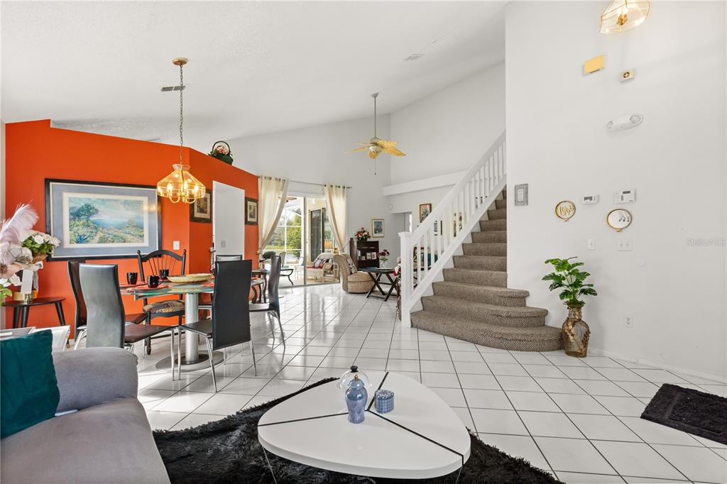 A living and dining area with white tile floors, a staircase, and an orange accent wall — 2703 CHATHAM, KISSIMMEE, FL
