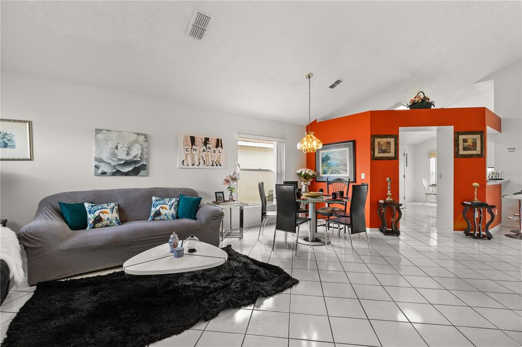 A living and dining area features white tile floors, a grey sofa, and orange accent walls — 2703 CHATHAM, KISSIMMEE, FL