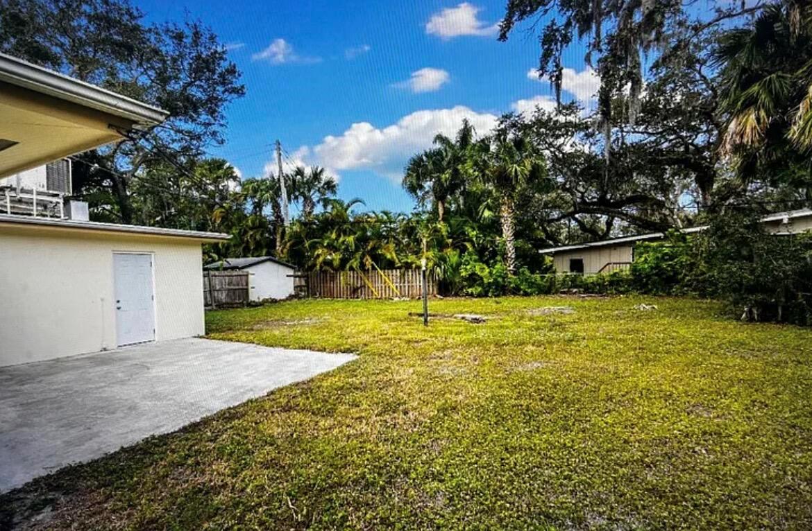 A grassy backyard features a concrete patio, a white storage shed, and mature palm trees — 515 Cypress Road, Vero Beach FL 32963, VERO BEACH, FL