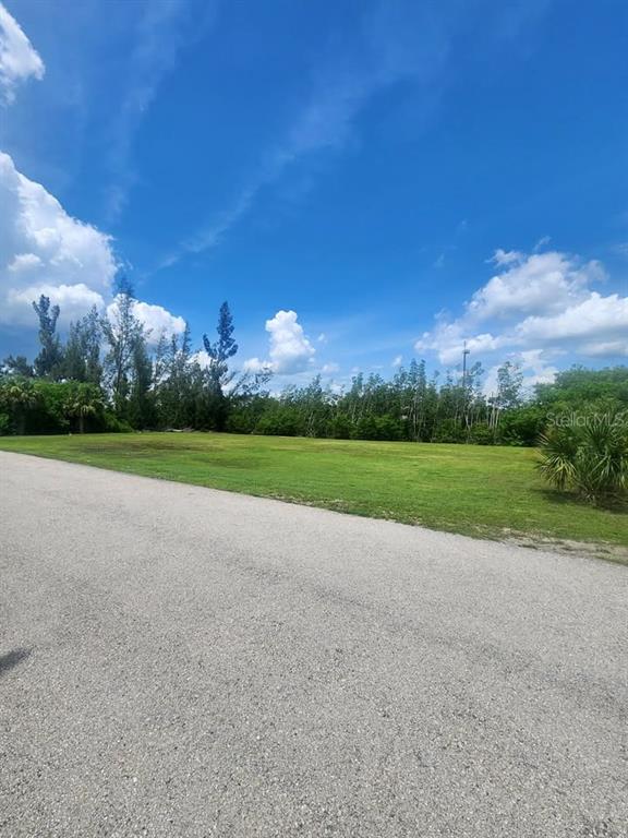 A vacant, grassy lot sits beside a paved road under a blue sky — 6146 LANDINGS WAY, PUNTA GORDA, FL