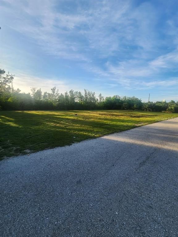 A vacant, grassy residential lot sits adjacent to a paved road under a blue sky — 6146 LANDINGS WAY, PUNTA GORDA, FL