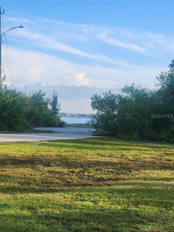A grassy lot leads toward a view of the water framed by trees and bushes — 6146 LANDINGS WAY, PUNTA GORDA, FL